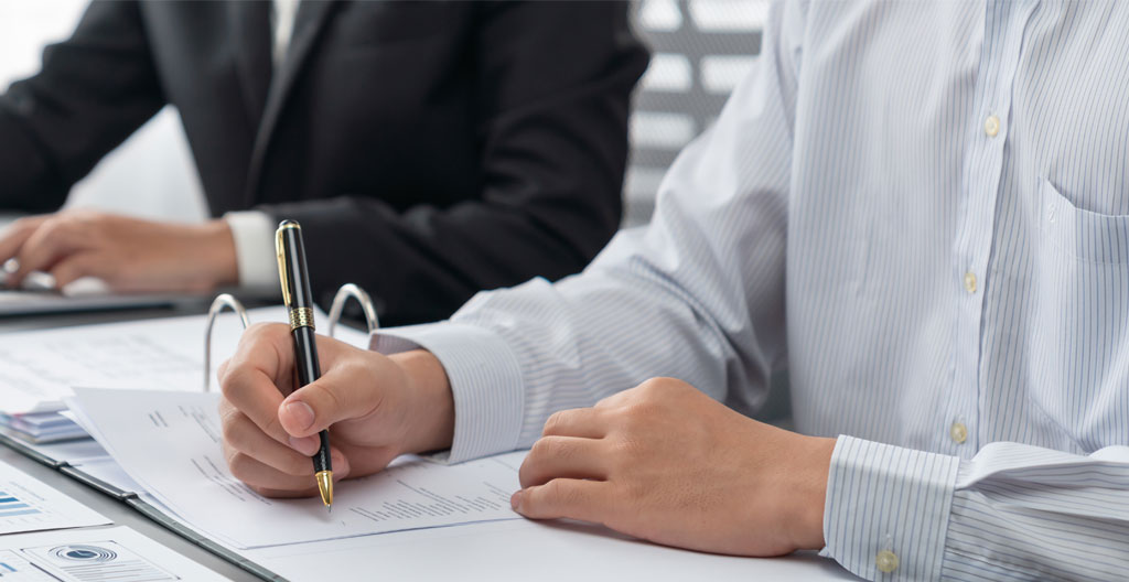 Gros plan sur une main tenant un stylo au-dessus d'un document de contrat de crédit automobile posé sur un bureau blanc moderne