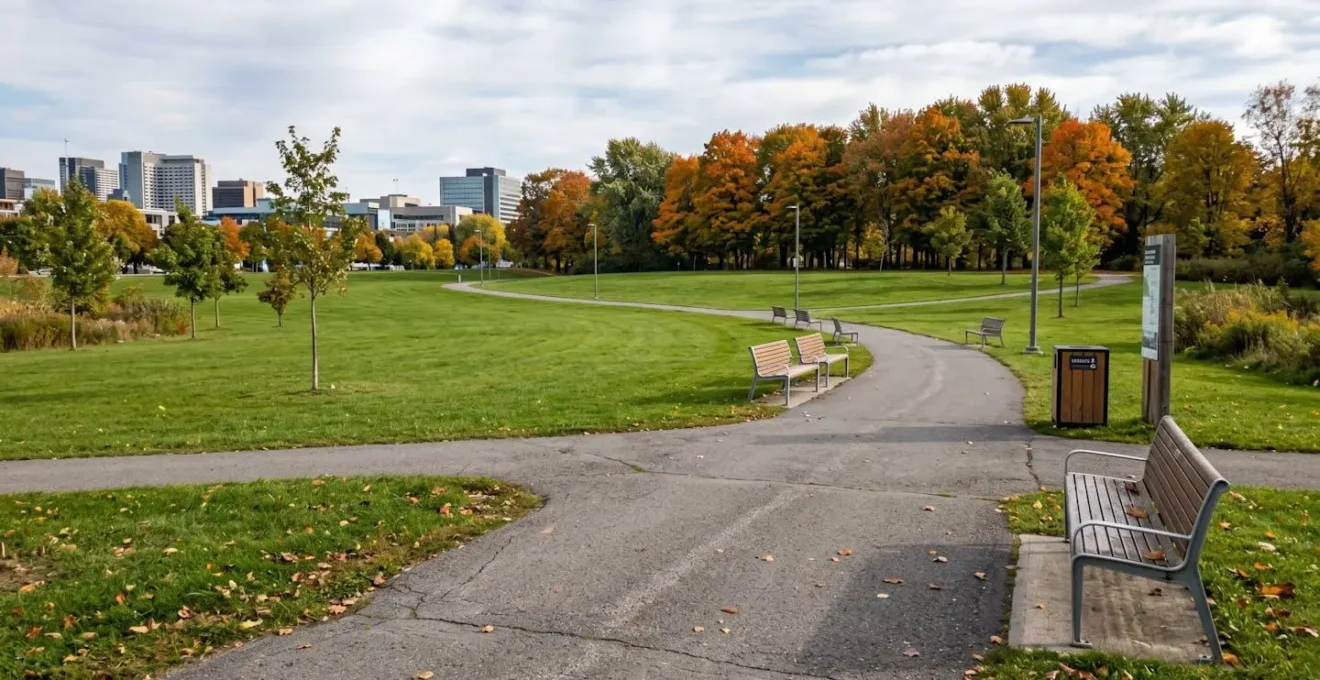 Vue grand angle d'un parc public urbain québécois avec vaste pelouse centrale et sentiers pavés, sans présence humaine, arbres matures en arrière-plan